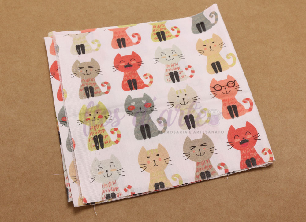 Pano de tecido branco com padrão de gatos coloridos sobre superfície castanha