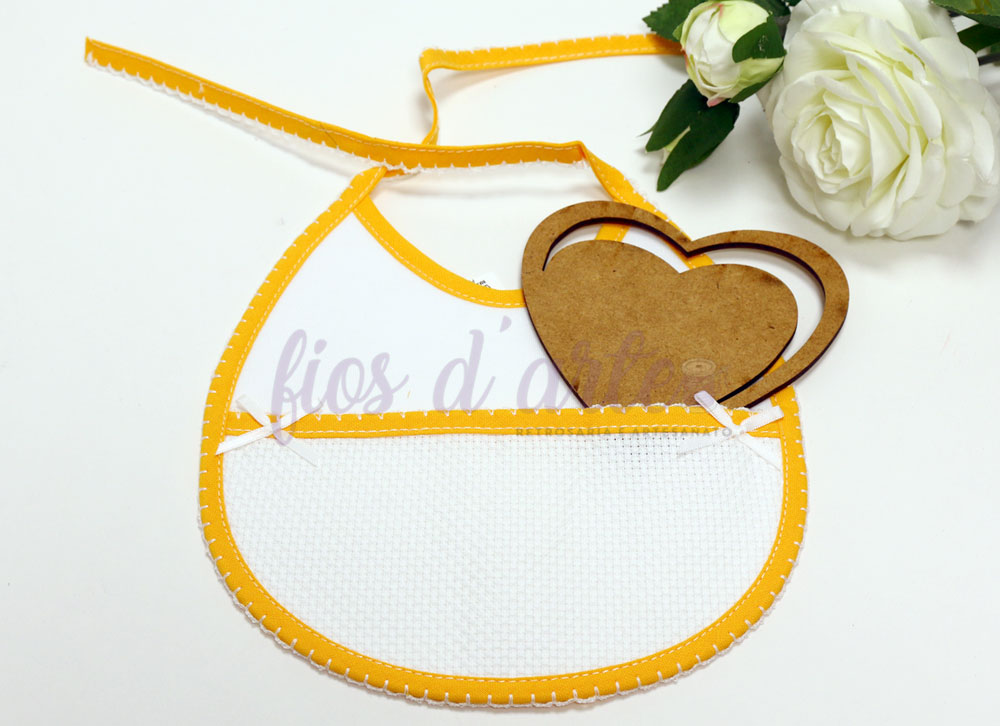 Babete branco com borda amarela e coração de madeira ao lado