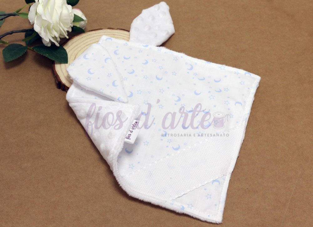 Doudou/ Naninha Orelhinhas com minky para bordar ponto cruz #09 (Fios d'arte) Pano de boca branco com padrão azul de luas e estrelas e textura de bolinhas em relevo.