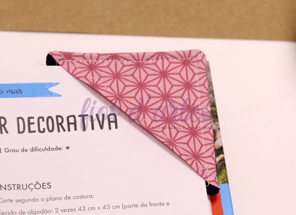 Marcador de livros em tecido rosa com padrão geométrico sobre página de livro em português