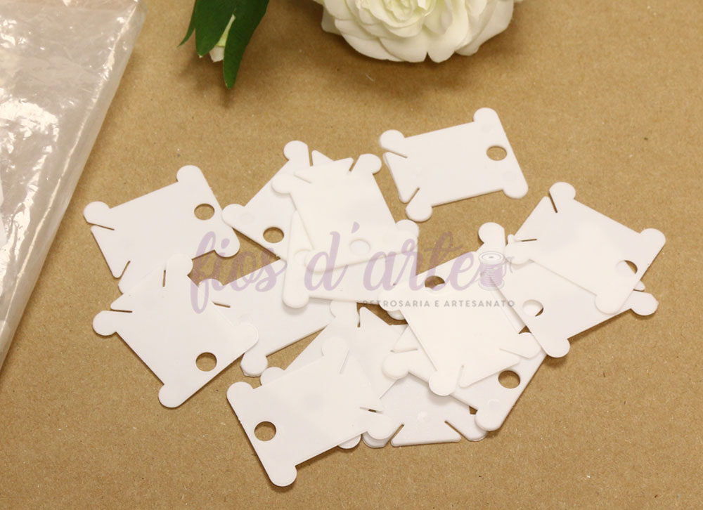 Plaquinha em plástico para enrolar linhas Placas brancas de plástico com recortes sobre mesa castanha com flor branca e texto de fundo