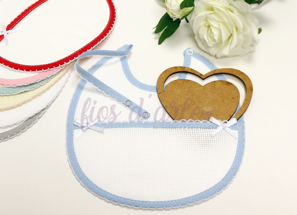 Seis babetes coloridos em tecido com renda e laços, com coração de madeira e flores brancas ao fundo