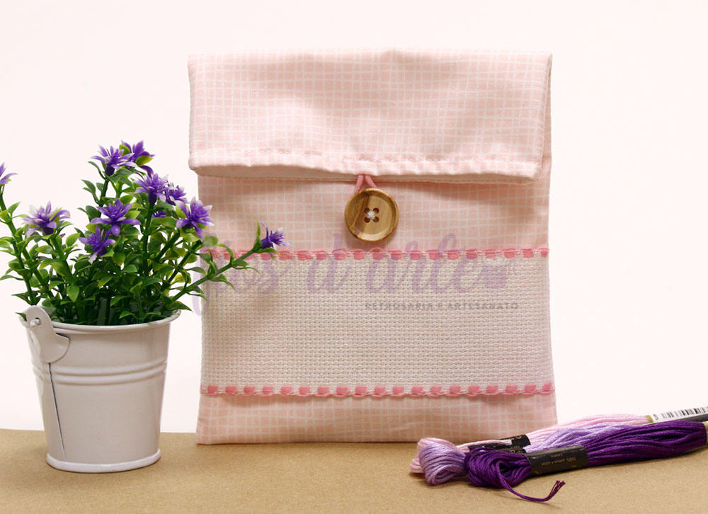 Estojo de tecido rosa com botão de madeira, planta artificial em vaso branco e fios de bordado roxos