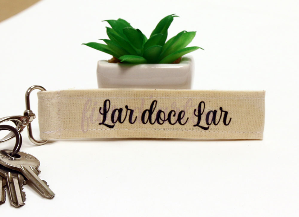 Porta-chaves de tecido com texto 'Lar doce Lar' junto a planta suculenta em vaso branco