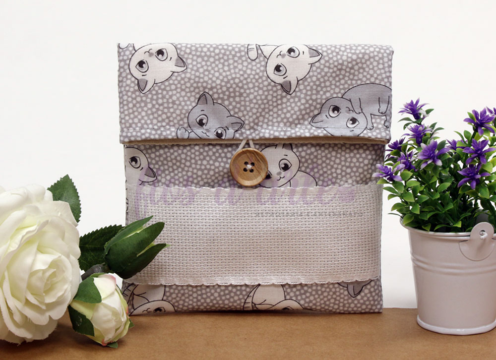 Bolsa de tecido cinzento com padrão de gatos e botão de madeira entre flores artificiais