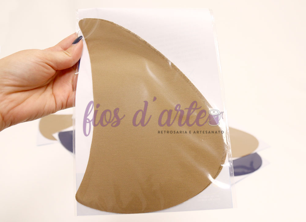 Item em forma de meia-lua bege claro dentro de embalagem transparente segurada pela mão.