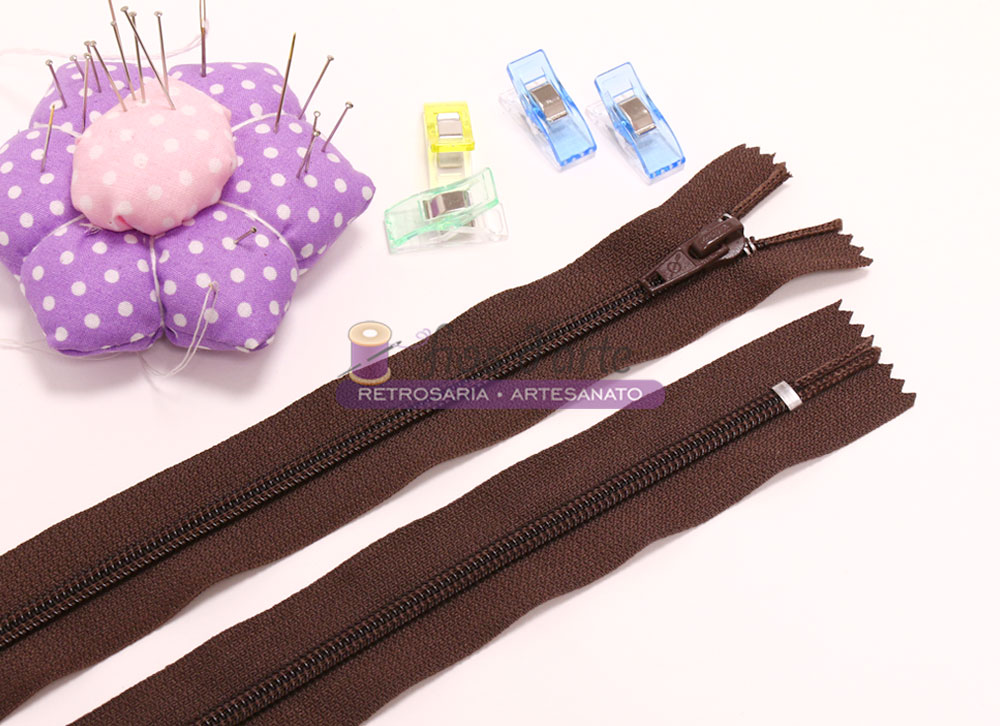 fechos éclair marrons, almofada de alfinetes roxa com pontos brancos, bobina de linha e pregadores coloridos