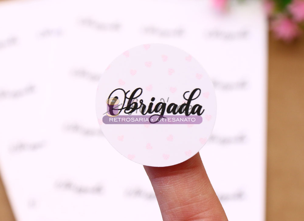 Etiqueta adesiva redonda Obrigada (Fios d'arte) Adesivo redondo branco com texto Obrigada e Retrosaria e Artesanato segurado no dedo