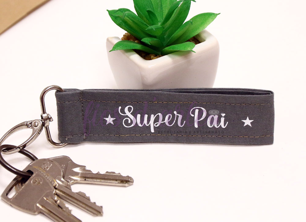 Porta-chaves em tecido ⭐Super Mãe/ Pai/ Avó/ Avô⭐ Porta-chaves cinzento com texto Super Pai, três chaves metálicas e planta verde em vaso branco.