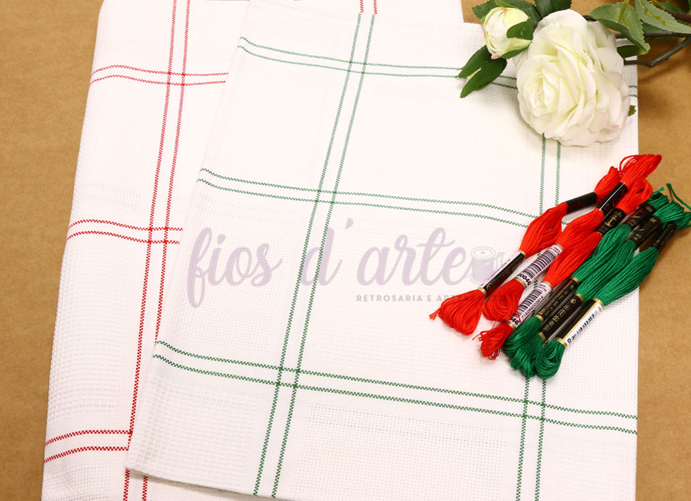 Tecido branco com linhas verdes e vermelhas, novelos de linha vermelha e verde, com flor branca.