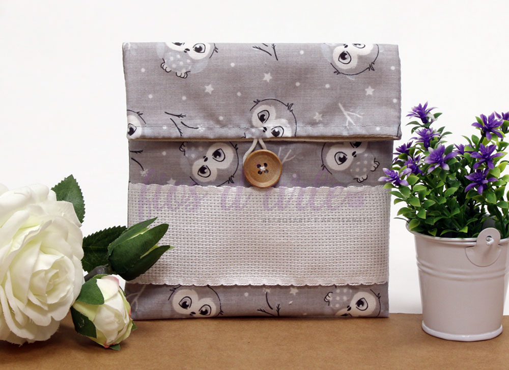 Bolsa Multiusos estampada com quadrilé para bordar ponto cruz (14x15cms) - cinzento com corujinhas Estojo cinza com padrão de corujas e botão de madeira ao centro, rodeado por flores brancas e lilases.
