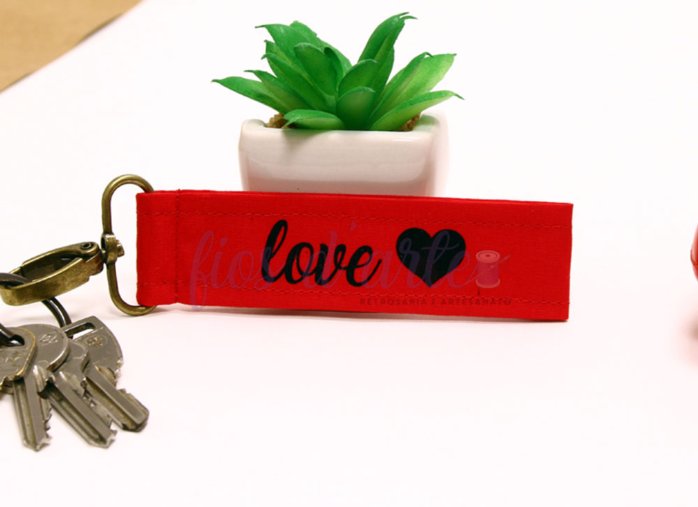 Chaveiro vermelho com palavra 'love' e coração preto junto a chaves e planta em vaso branco