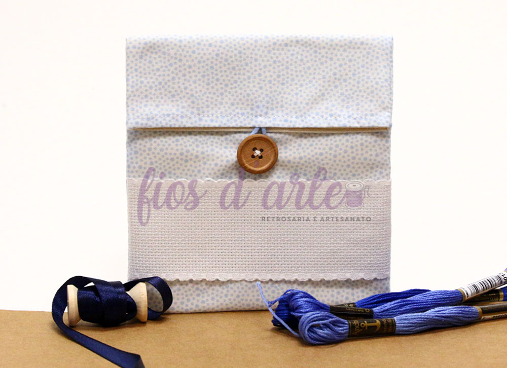 Envelope artesanal bege com botão de madeira e linha azul sobre mesa