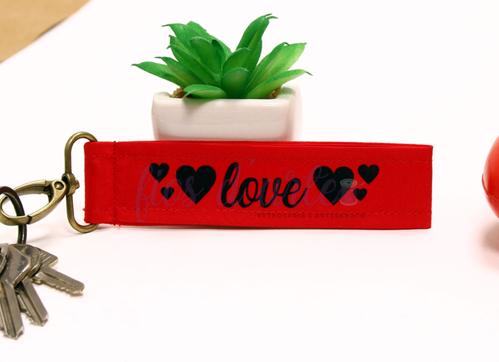 Chaveiro vermelho com estampa 'love' e corações pretos próximo a uma planta suculenta