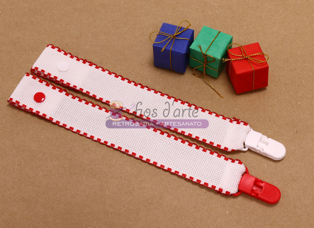 Prende-chupeta com fita em quadrilé para bordar ponto cruz #5 (Fios d'arte) Dois clips para chupeta brancos com detalhes vermelhos junto a três pequenas caixas coloridas