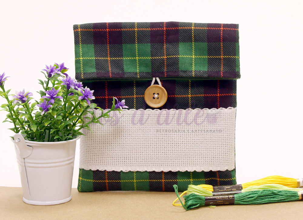 Bolsa xadrez verde com botão e faixa branca, flores roxas em vaso branco, novelos de linha verde e amarelo