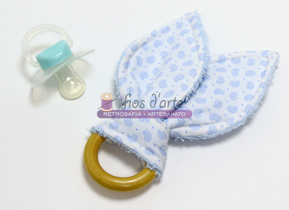 Mordedor Orelhas de Coelho (branco cornucópias azuis) Anel de dentição com tecido azul claro e chucha azul claro sobre superfície branca
