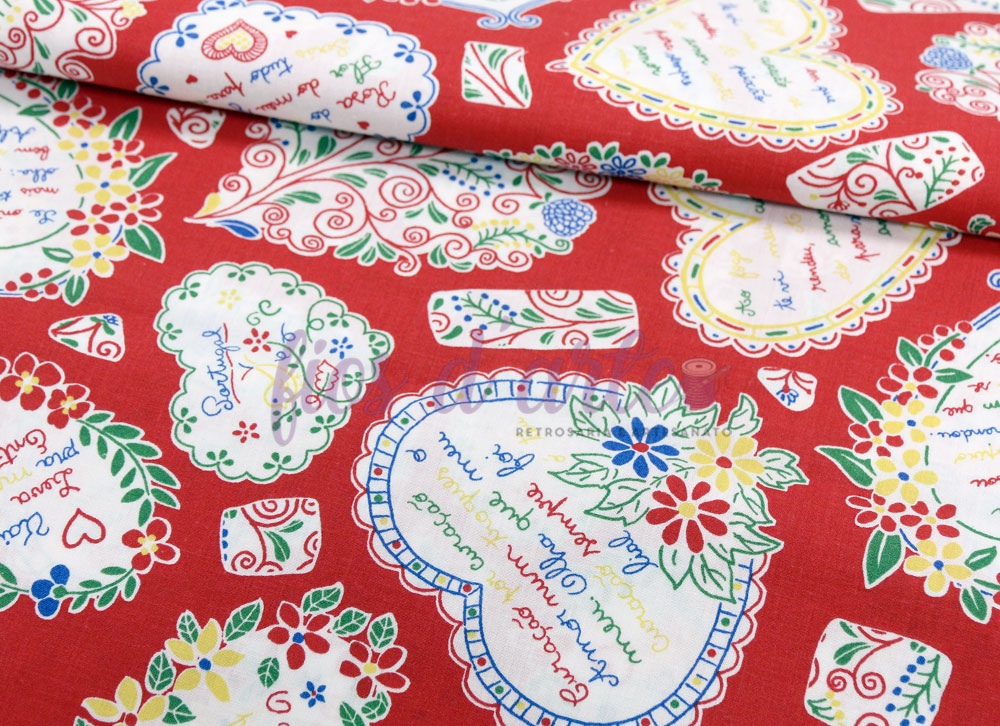 Tecido vermelho com corações brancos decorados e texto colorido em padrão repetitivo