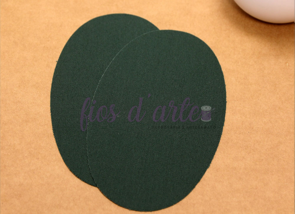 Joelheiras/ Cotoveleiras Termocolantes - verde militar Dois ovais verdes escuros texturizados com texto 'fios d'arte' em roxo sobre superfície castanha