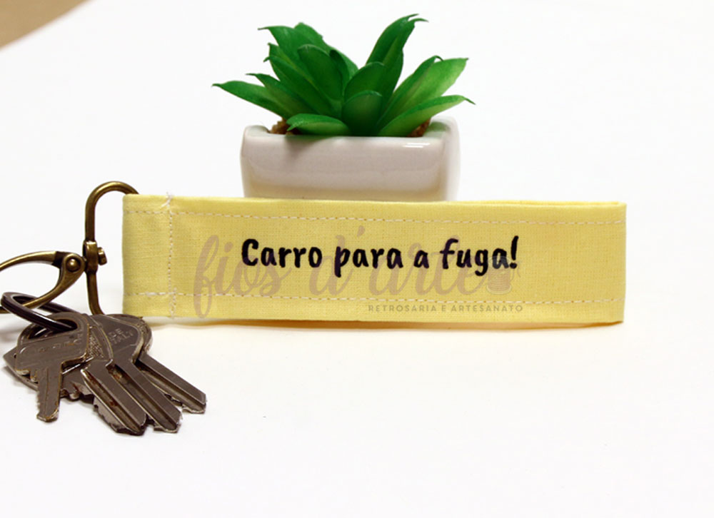 Chaveiro amarelo com texto e chaves ao lado de planta suculenta