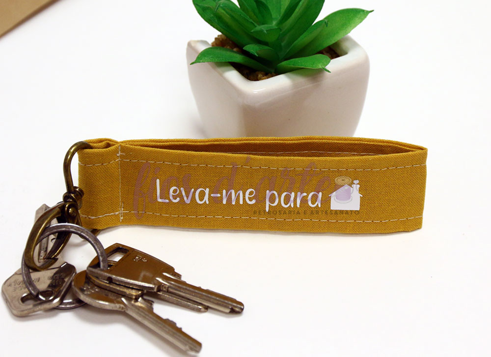Porta-chaves de tecido amarelo com frase e imagem de uma cama, com chaves e vaso com planta