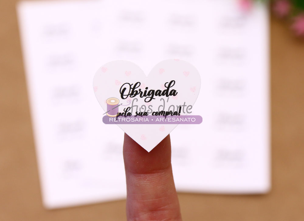 Etiqueta adesiva coração Obrigada pela sua compra (Fios d'arte) Etiqueta em forma de coração com texto de agradecimento colocada na ponta do dedo