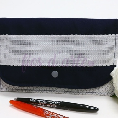 Bolsa de tecido azul escuro com faixa branca translúcida e botão de pressão, canetas, ganchos e flor