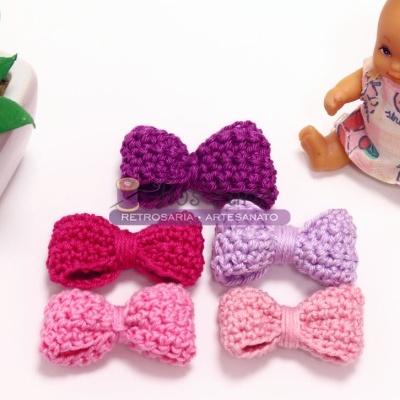 Cinco laços de crochê rosa e roxo com boneco e planta em vaso branco