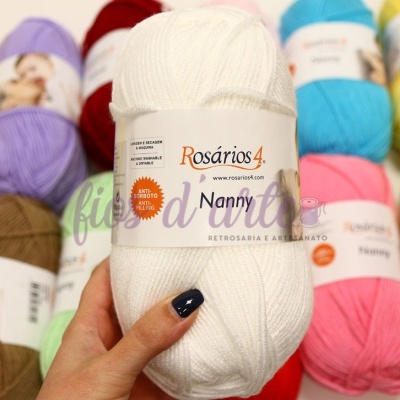 Novelo de lã branca Rosários 4 Nanny segurado com outros novelos coloridos ao fundo