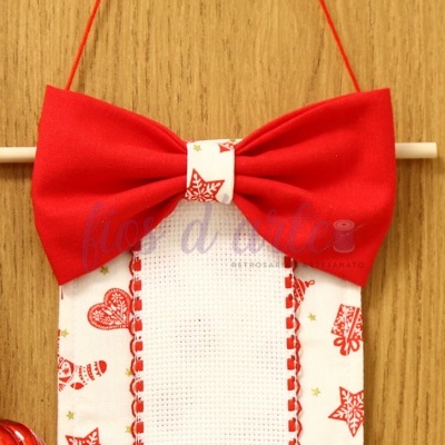 Expositor de tecido com laço vermelho e bordado vermelho em fundo de madeira clara