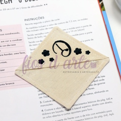 Envelope tecido bege bordado relógio nuvens pássaro em página com texto em português