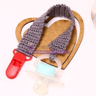 Chupeta com clip e fita tricotada cinza sobre suporte de coração de madeira
