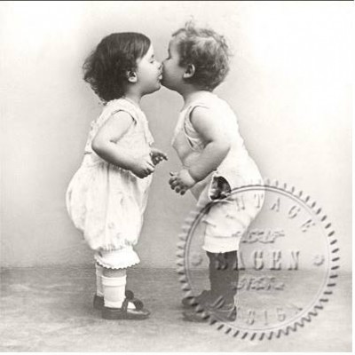 Duas crianças pequenas em macacões brancos num beijo, fundo neutro, carimbo redondo visível