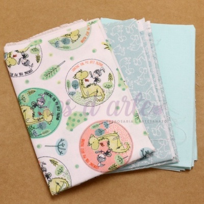 Três tecidos dobrados com padrões infantis e cores azul e branco sobre fundo castanho.