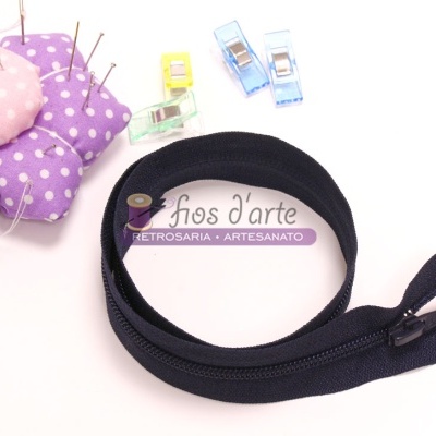 Fecho éclair preto enrolado com alfineteiro roxo, almofada rosa e molas de costura coloridas.