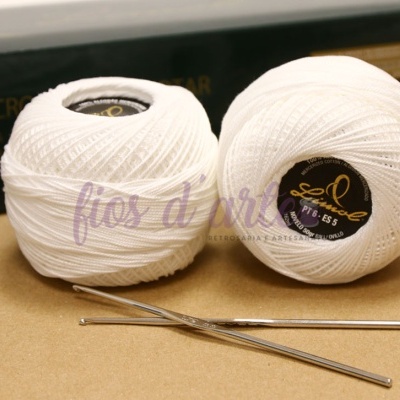 Dois novelos de linha branca com etiquetas pretas e agulhas de croché sobre superfície castanha