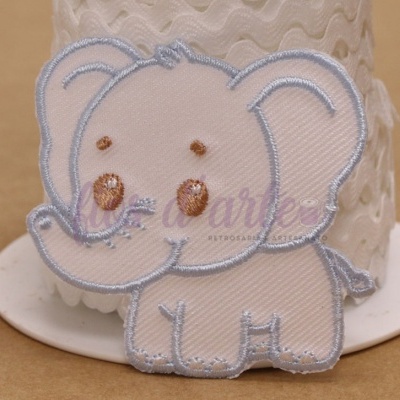 Bordado de elefante cor de creme com contornos cinzentos em frente a um rolo de fita branca