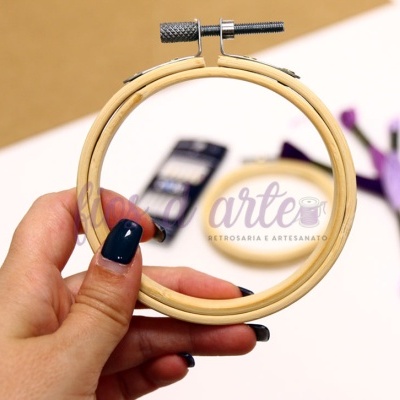 Bastidor de madeira para bordado com texto 'arte' visível ao fundo