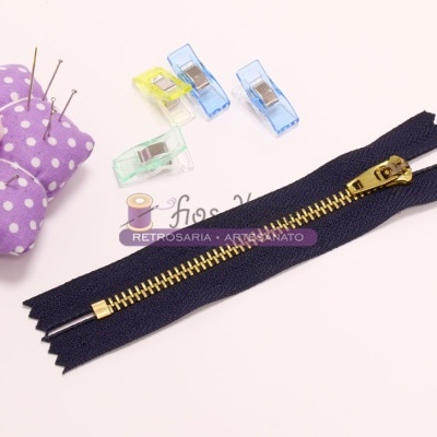 Fecho éclair preto com dentes dourados, prendedores de tecido coloridos e alfineteiro flor roxa