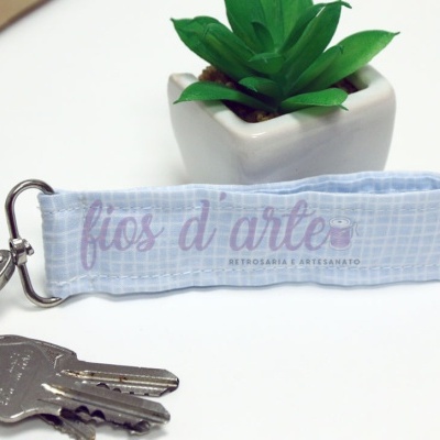 Chaveiro azul claro em tecido com padrão quadrado e chave, planta artificial em vaso branco