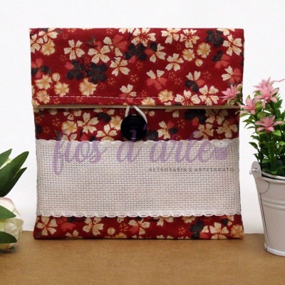 Carteira em tecido floral vermelho com botão preto, junto a flores brancas e cor-de-rosa em vaso branco