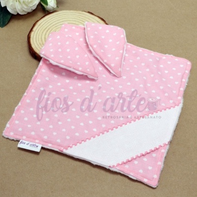 Toalha rosa com corações brancos e orelhas de tecido sobre superfície castanha com base de madeira e flor branca