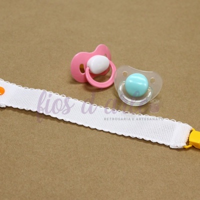 Duas chupetas e um prendedor de chupeta em fundo castanho.