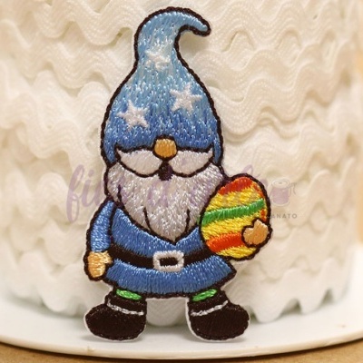 Patch bordado de gnomo azul segurando ovo colorido colocado em rolo de fita branca