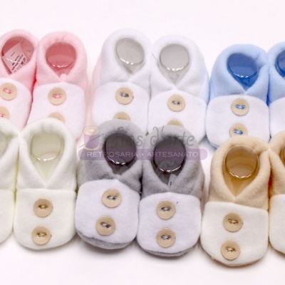 Seis pares de sapatinhos de bebé em várias cores com botões, organizados em duas filas sobre fundo branco