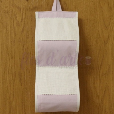 Suporte em tecido branco e lilás para rolo de papel pendurado numa parede de madeira.