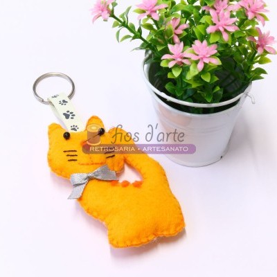 Chaveiro de gato laranja de feltro ao lado de vaso branco com flores cor-de-rosa