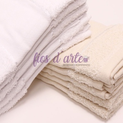 Duas pilhas de toalhas de banho dobradas, branca e bege, em fundo branco