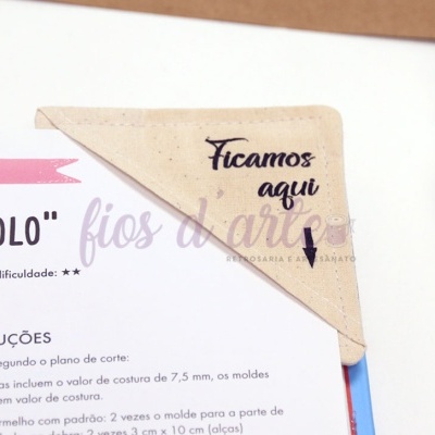 Guardanapo de tecido bege com texto 'Ficamos aqui' e seta em superfície com documento impresso