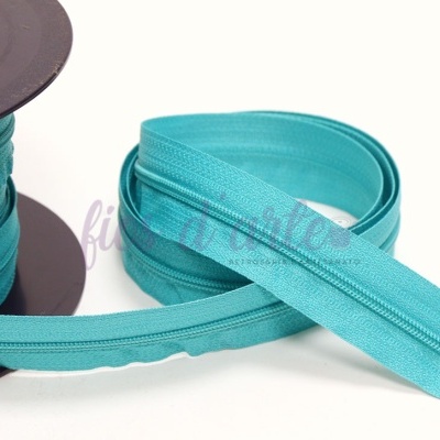 Rolo de zipper turquesa, parcialmente desenrolado sobre fundo branco.